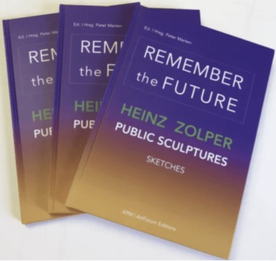 Three copies of the book "Remember the Future: Heinz Zolper Public Sculptures, Sketches" are arranged in a fan shape. The covers are purple and gold with white and green text.