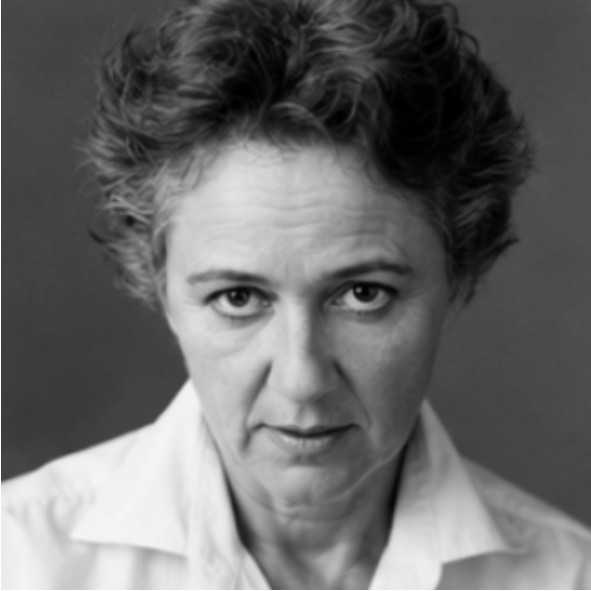 A black and white portrait of a person with short, curly hair, wearing a light-colored collared shirt, looking directly at the camera with a serious expression against a plain background.