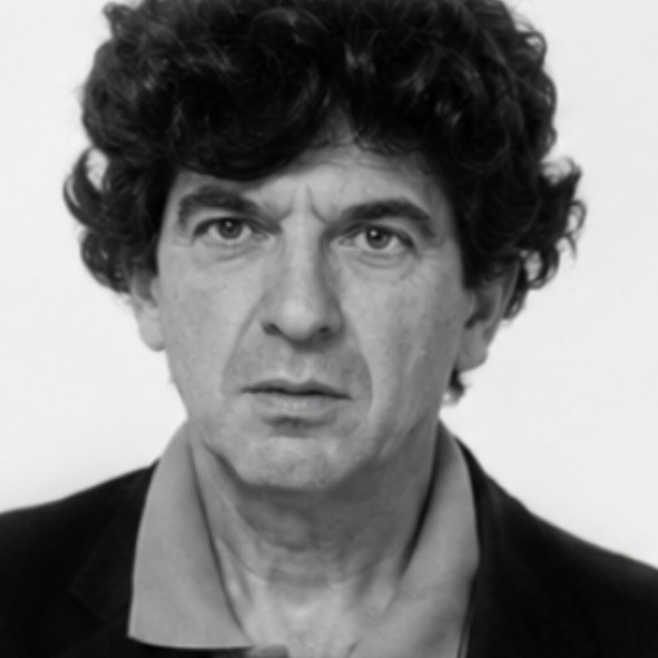 A black and white close-up portrait of a man with curly dark hair and a serious expression. He is wearing a collared shirt and a jacket.