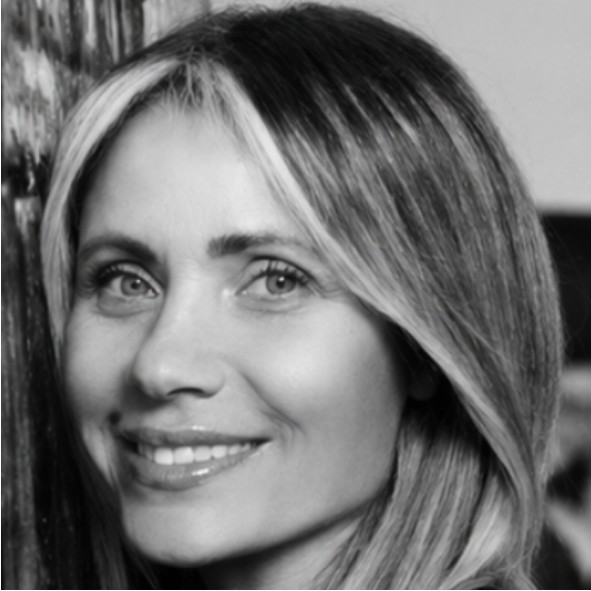 Black and white close-up photo of a woman with long, straight hair featuring light and dark streaks, smiling softly while looking slightly past the camera.