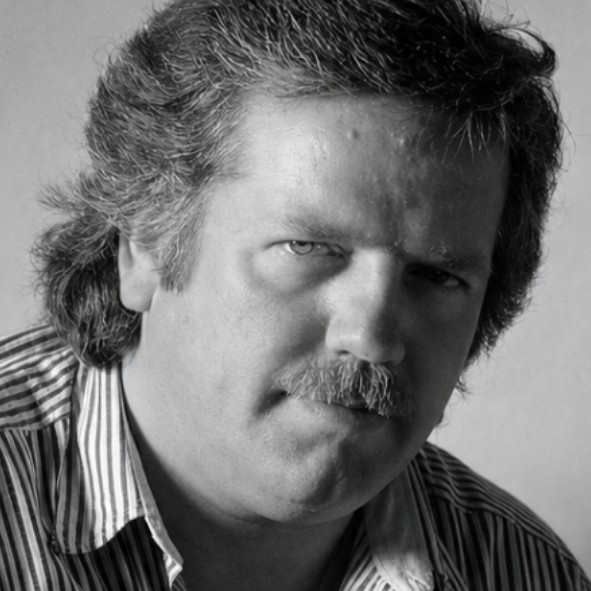 Black and white portrait of a middle-aged man with wavy hair and a mustache, wearing a striped shirt, looking directly at the camera with a serious expression.