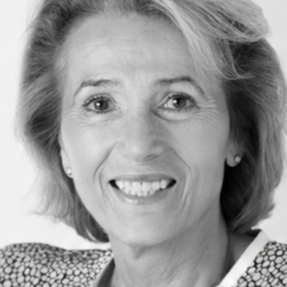 Black and white portrait of an older woman with light hair, wearing a patterned jacket and small earrings, smiling at the camera against a plain background.
