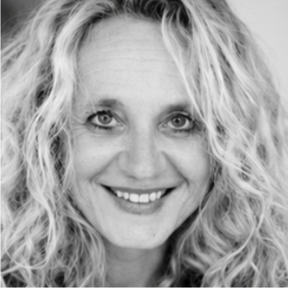 Black and white portrait of a smiling woman with long, curly hair, looking directly at the camera. The background is softly blurred.