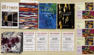 A display of art books and flyers on a table, featuring colorful abstract covers by Jana Dettmer, Corinna Zieleke, and Leona J. Aerni, along with “New Feminism” event flyers arranged neatly in rows.